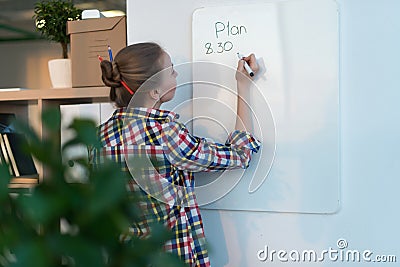 Young woman writing day plan on white board, holding marker in right hand. Student planning schedule rear view portrait Stock Photo