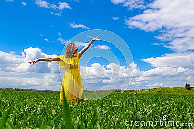 Young woman in yellow dress outdoors in green field. The concept of love of life and openness to the world Stock Photo