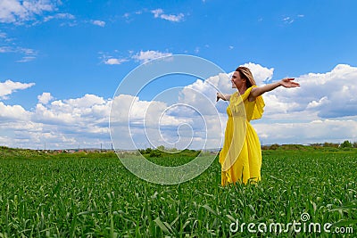 Young woman in yellow dress outdoors in green field. The concept of love of life and openness to the world Stock Photo