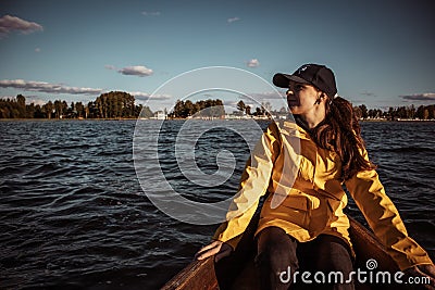 Young woman in yellow raincoat and cap sitting on a boat and looking afield Stock Photo