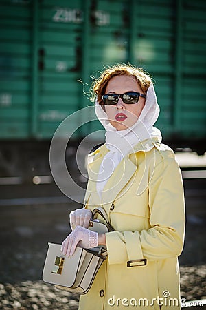 A young woman in a yellow raincoat and dark glasses, with an open handbag in her hands Stock Photo