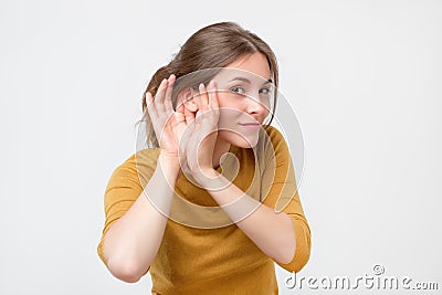 Young woman in yellow sweater listening to gossip about other with hand near ear. Stock Photo