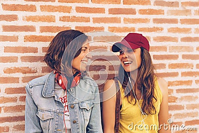 Young women couple looking and smiling each other in a brick wall background. Same sex happiness and joyful scene Stock Photo