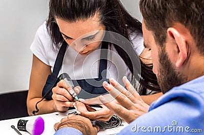Young woman doing manicure to a man. A man in a shirt and with a beard looks at his hand Stock Photo