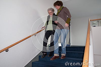 Caregiver helping senior woman walking down the stairs Stock Photo