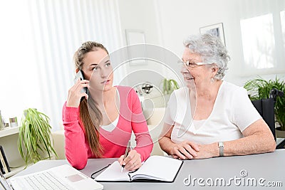Young woman helping an old senior woman doing paperwork and administrative procedures with laptop computer at home Stock Photo