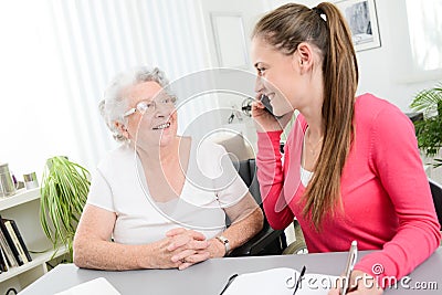 Young woman helping an old senior woman doing paperwork and administrative procedures with laptop computer at home Stock Photo