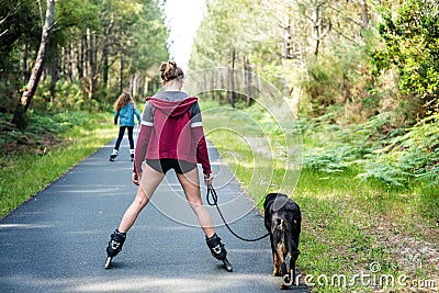 young woman rollerblading with her dog on a cycle path crossing the forest Stock Photo
