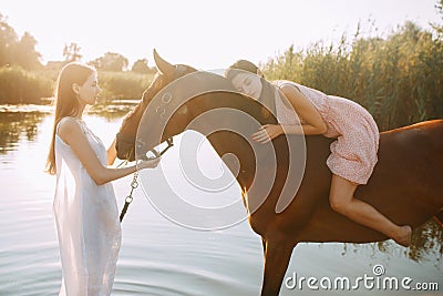 Woman lies astride a horse and other woman stands nearby Stock Photo