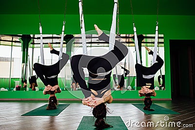 Young women making antigravity yoga exercises with a group of people. aero fly fitness trainer workout. white hammocks. Stock Photo