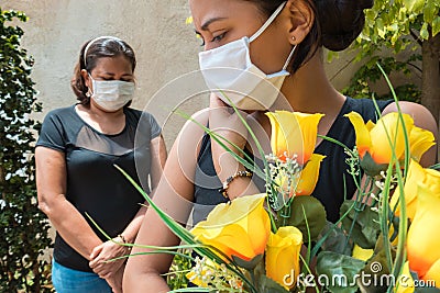 Young woman in mourning, dressed in black with flowers and chewing. Masked people at a funeral Stock Photo