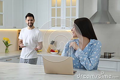Young woman in pajamas using laptop while boyfriend bringing coffee at home Stock Photo
