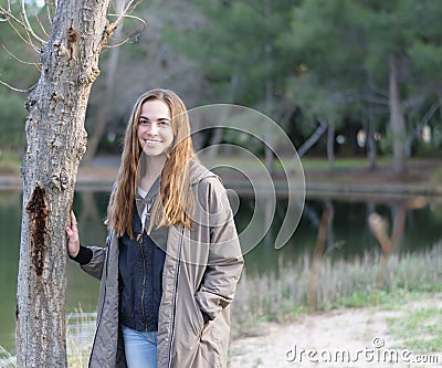 Young women poses outdoors next to a tree and lake Stock Photo
