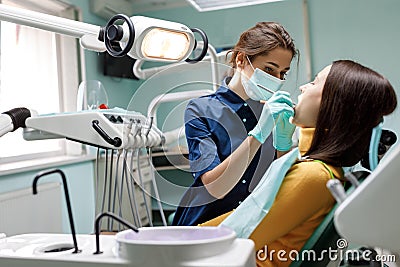 The beautiful young woman is at the dentist. She sits in the dentist`s chair and the dentist carefully examines the patient`s Stock Photo