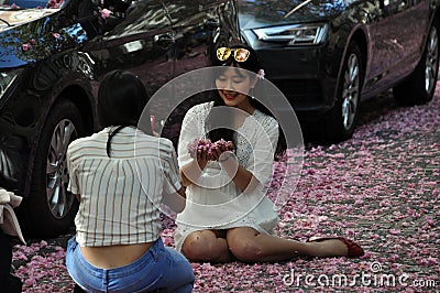 Young women sitting on road covered with red rose cherry blossoms Editorial Stock Photo