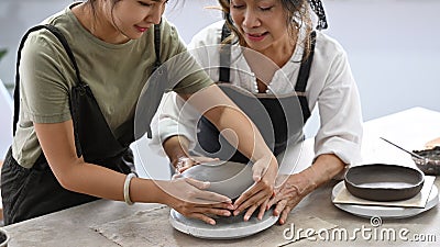 Young woman teaching mature woman making ceramic pot from clay in pottery workshop. Activity, handicraft, hobbies Stock Photo
