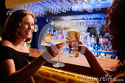 Young women in evening dress smiling during celebratory toast with drinks at bar Stock Photo