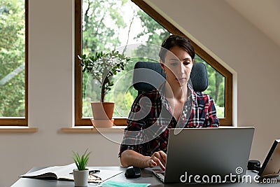 Young women working from home. Sitting in attic with laptop near roof window. New normal concept Stock Photo