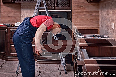 A young worker installs a drawer. Installation of modern wooden kitchen furniture Stock Photo