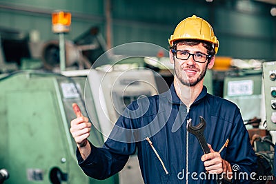 Young worker with wrench repair engineer fix machine happy smiling in factory hand thumb up for good job signal Stock Photo