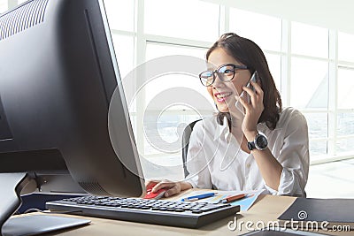 Young working woman talking to phone with watching on computer o Stock Photo