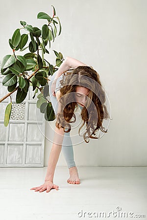 Young yogini practicing in a room with white walls and plant Stock Photo