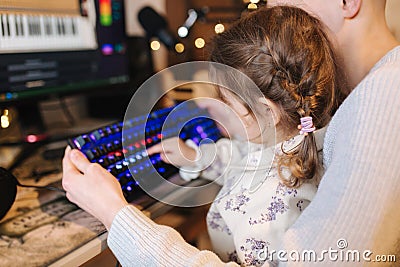 Younger sister sits on brothers knees and put finger on keyboard with neon light. Little girl help brother work on Stock Photo