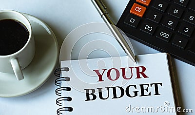 YOUR BUDGET - words written in a notebook against the background of a calculator and a cup of coffee Stock Photo