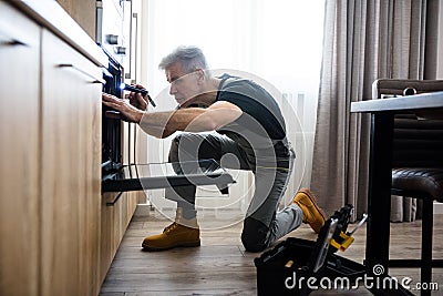 Your personal technician. Full length shot of aged repairman in uniform working, examining broken oven in the kitchen Stock Photo
