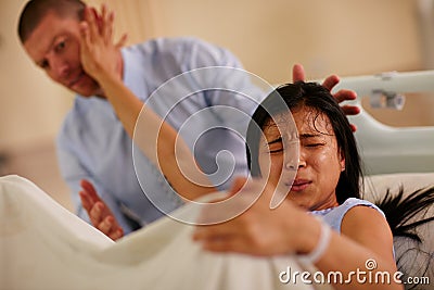 Youre not helping.... Shot of a young woman giving birth with her husband supporting her in the background. Stock Photo