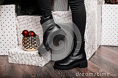 Youth fashionable leather black women`s winter boots. Young woman in jeans in trendy shoes stands in a room near the holiday boxe Stock Photo
