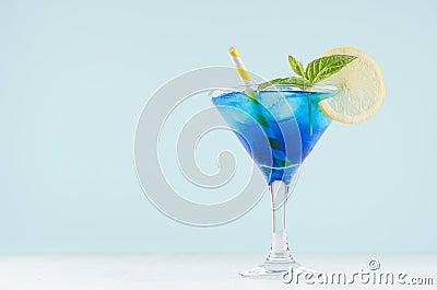 Youth fresh alcohol blue Hawaii cocktail with licor curacao, ice cube, lemon slice, yellow straw in wine glass on mint background. Stock Photo