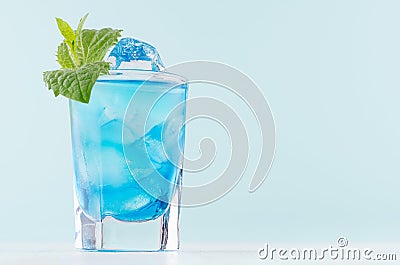 Youth fresh alcohol blue Hawaii cocktail with liquor curacao, ice cube, green mint in shot glass on elegant pastel mint background Stock Photo