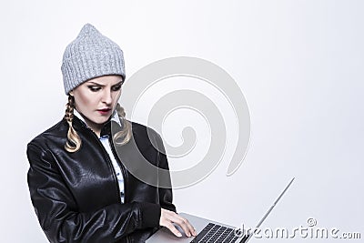 Youth Lifestyles. Caucasian Blond Femalr in Warm Hat and Leather Jacket Posing With Laptop With Ingratiating facial Expression on Stock Photo