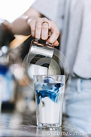 A youthful pretty slim blonde,wearing casual outfit, pours coffee into a glass of milk in a cozy coffee shop. Stock Photo