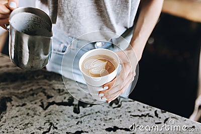 A youthful slim kind blonde girl,dressed in casual outfit,skillfully adds milk to coffee in a modern coffee shop. Stock Photo