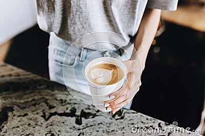 A youthful slim kind blonde girl,dressed in casual outfit,skillfully adds milk to coffee in a modern coffee shop. Stock Photo