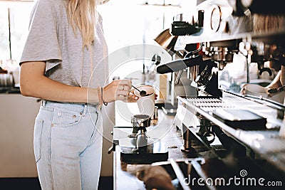 A youthful thin blonde lady,wearing casual clothes,stands nexrt to the coffee machine in a cozy coffee shop. Stock Photo