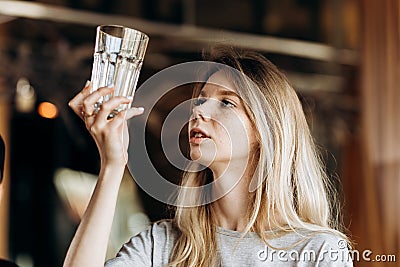 A youthful thin blonde,wearing casual outfit,is looking attentively at the clean glass in a cozy coffee shop. Stock Photo