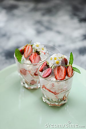 Yummy British dessert Eton mess with raw strawberries, cream and meringues in glasses in green plate side view Stock Photo