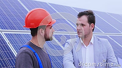 Zakenman die aan een arbeider op een achtergrond van zonnepanelen spreken Zakenman die aan een arbeider op een achtergrond van zonnepanelen spreken