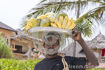 African man holds fresh tropical fruits for sale for tourist on the head near beach of Zanzibar island, Tanzania, East Africa, Editorial Stock Photo