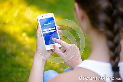 ZAPORIZHZHYA, UKRAINE - SEPTEMBER 20, 2014: Young Woman Using Facebook Social Network Application on her Smart Phone Editorial Stock Photo