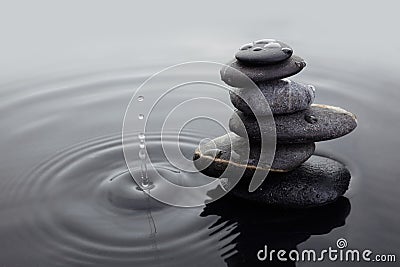Zen stones in balanced pile in water on rippled water surface and water drop. Stock Photo
