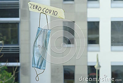 Zero covid sign and old surgical mask on window, office buildings in the back Stock Photo