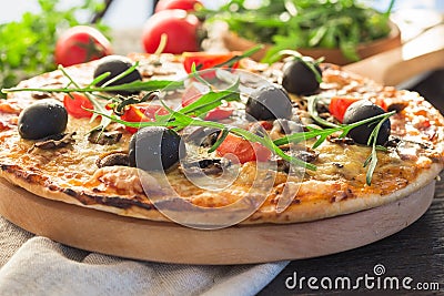 Flatbread pizza garnished with fresh arugula on wooden pizza board, top view. Dark stone background. Person picking slice of pizza Stock Photo