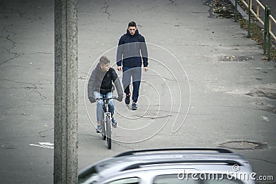 Zhytomyr, Ukraine - October 19, 2015: Young man wheeling bike in city near walking man Editorial Stock Photo