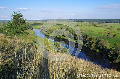 Zigzag river flows between summer valleys Stock Photo