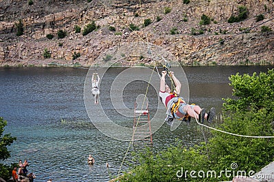 Zipline. The man in the equipment slides on a steel cable. Trolley Track Over the lake. Extreme Editorial Stock Photo