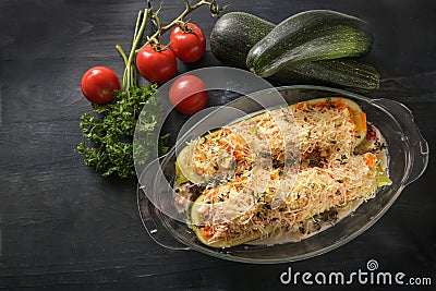 Zucchini filled with vegetables, feta cheese and parmesan in a glass baking casserole prepared for the oven, dark rustic wooden Stock Photo